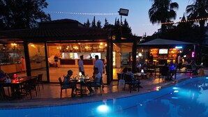 An outdoor pool area with a restaurant and bar, surrounded by palm trees and string lights. - Lemas Suite Hotel  (Manavgat)