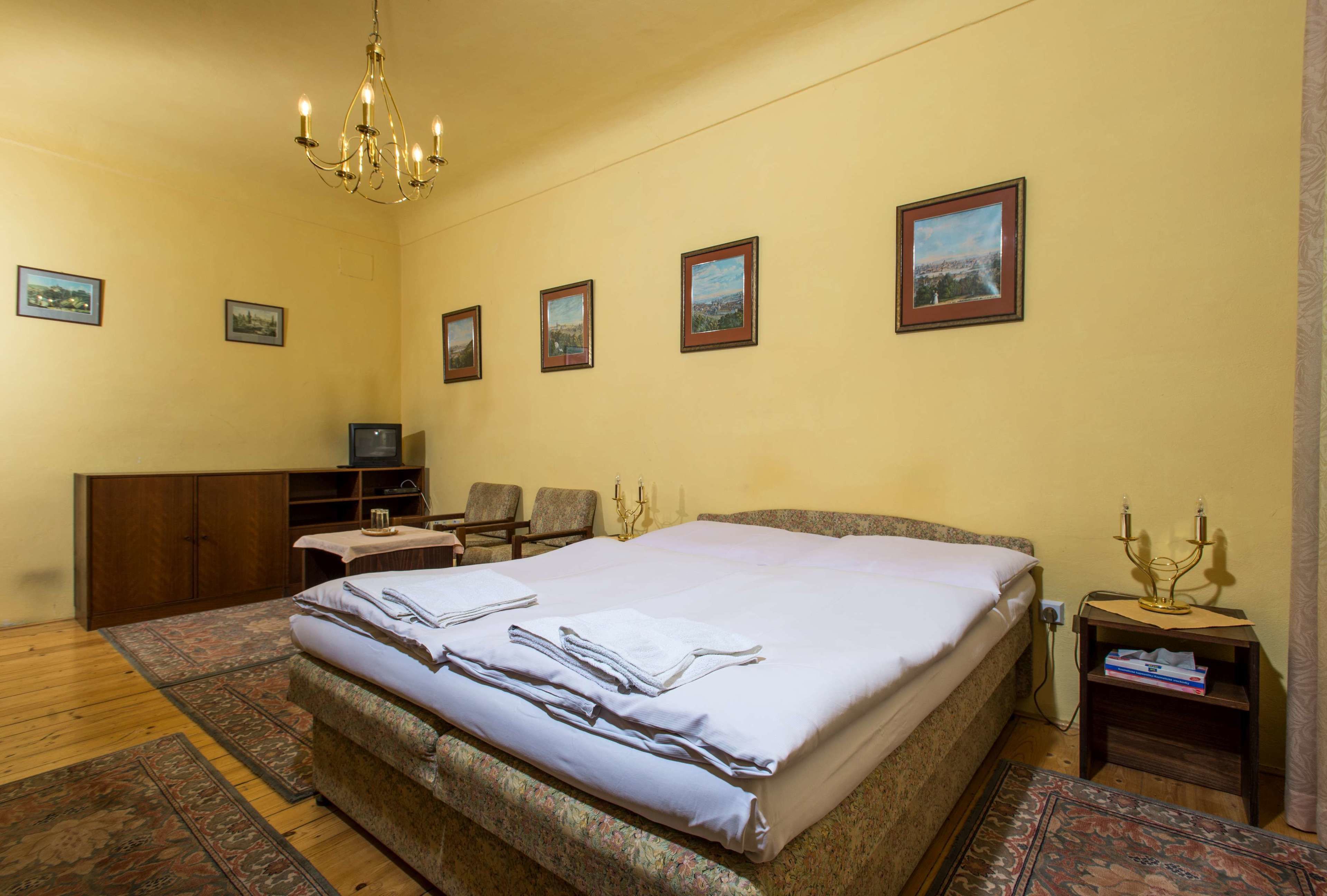 A hotel room with a large bed, a desk with a chair, a television, and framed pictures on the wall.
