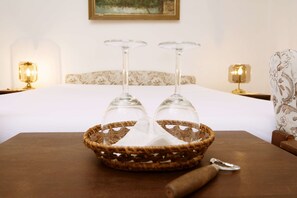 A neatly arranged room with a bed, two bedside lamps, a wicker basket with wine glasses, and a wooden table with a bottle opener. - Pension Dientzenhofer (Prague)