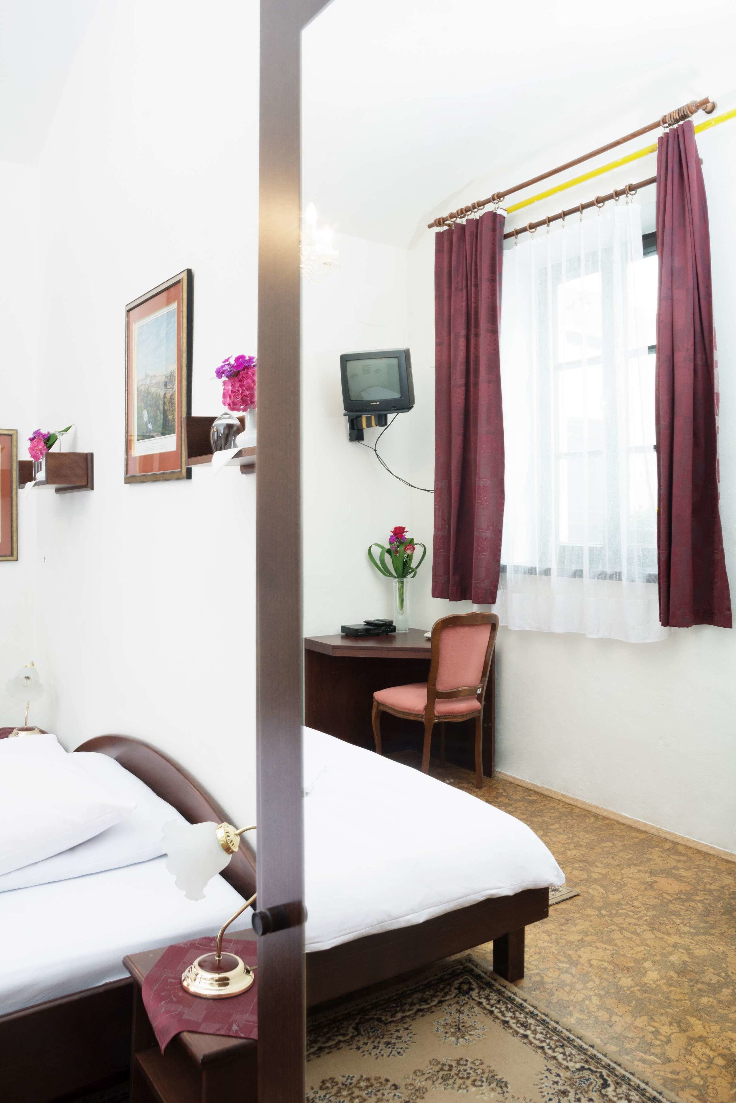 Habitación de hotel con cama, escritorio, silla, televisor y ventana con cortinas.