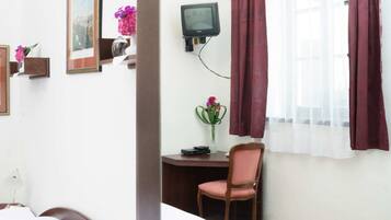 Habitación de hotel con cama, escritorio, silla, televisor y ventana con cortinas.