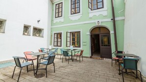 Un patio con mesas al aire libre, un edificio verde con varias ventanas y una puerta.
