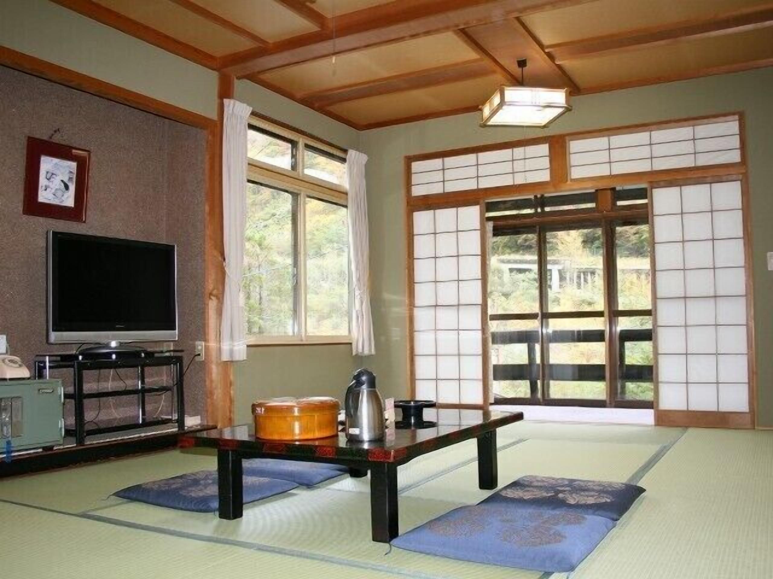 A tatami mat room with a television, a table with a kettle, and a view of the outdoors through shoji screens.