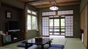 Una habitación japonesa tradicional con suelo de tatami, una mesa baja, cojines, televisión y puertas correderas.
