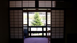 Una habitación japonesa tradicional con suelo de tatami, puertas correderas shoji y vista a un árbol.