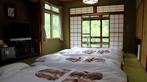 Una habitación tradicional japonesa con suelo de tatami, una cama futón con ropa de cama estampada, un televisor sobre un pedestal y un biombó shoji con vista a la vegetación.