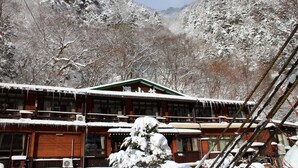 Un edificio de madera tradicional con múltiples ventanas y un techo cubierto de nieve, rodeado de árboles y montañas cargadas de nieve.