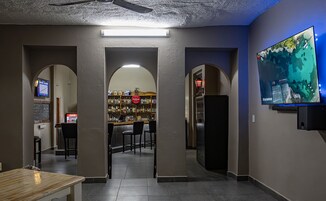 Zona de bar con mostrador, taburetes y una estantería llena de botellas de licores.