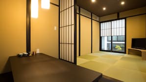 Una habitación japonesa tradicional con suelo de tatami, puertas correderas shoji, una mesa baja con una bandeja y un televisor sobre un soporte.