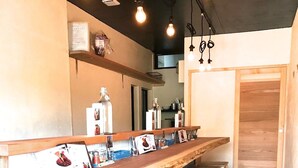 Una barra de madera larga con taburetes, una barra con varias botellas y vasos, y una puerta de madera al fondo.