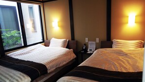 Habitación de hotel con dos camas, una ventana y una mesita de noche con teléfono y papeles.