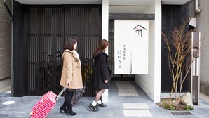 Dos personas caminando hacia un edificio con una entrada moderna y un letrero con caracteres japoneses.