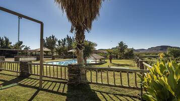 A backyard with a swing set, a stone wall, a pool, and a view of mountains.