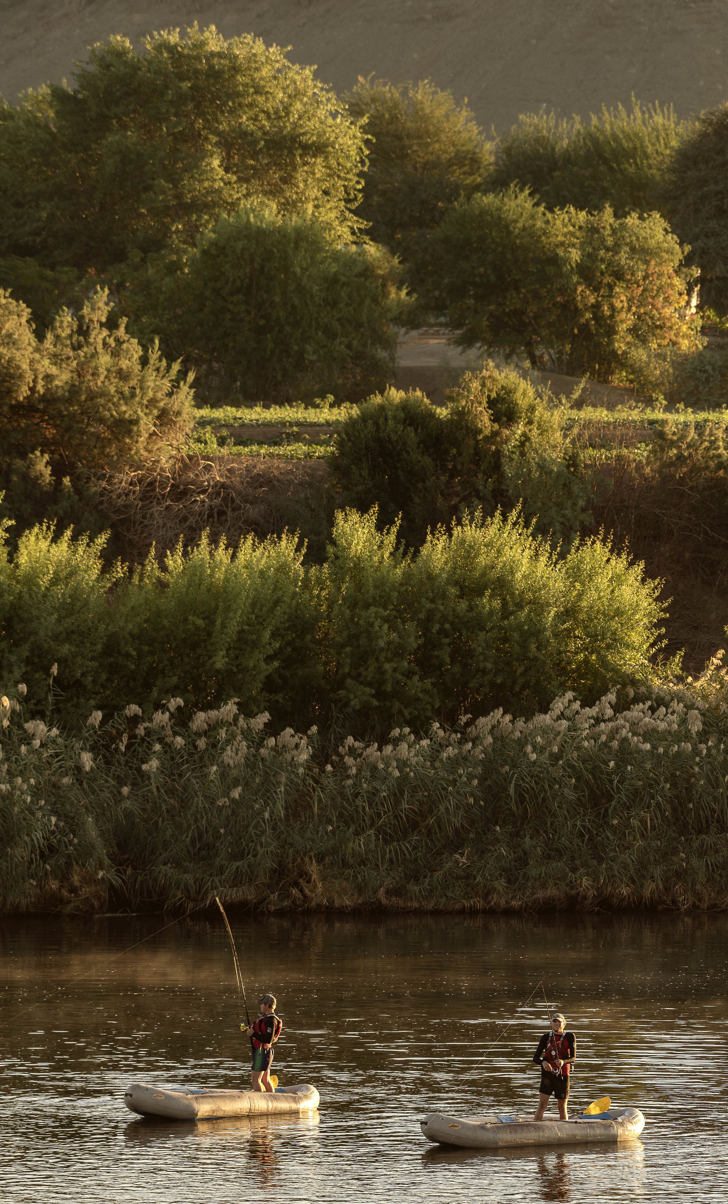 Two people on a raft in a river surrounded by dense vegetation.