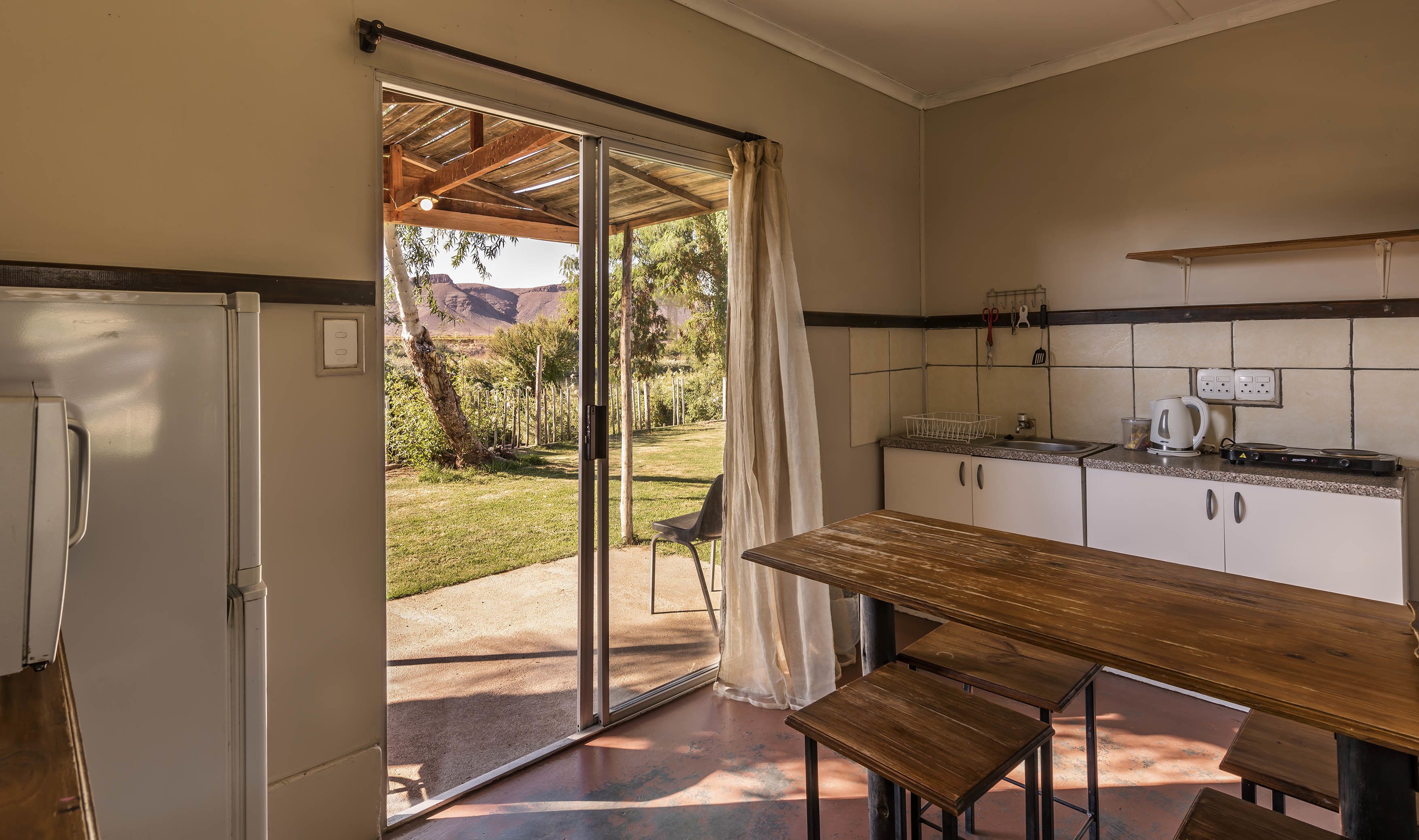 Una cocina con una mesa de madera y bancos, un refrigerador y vistas a un jardín a través de un ventanal.