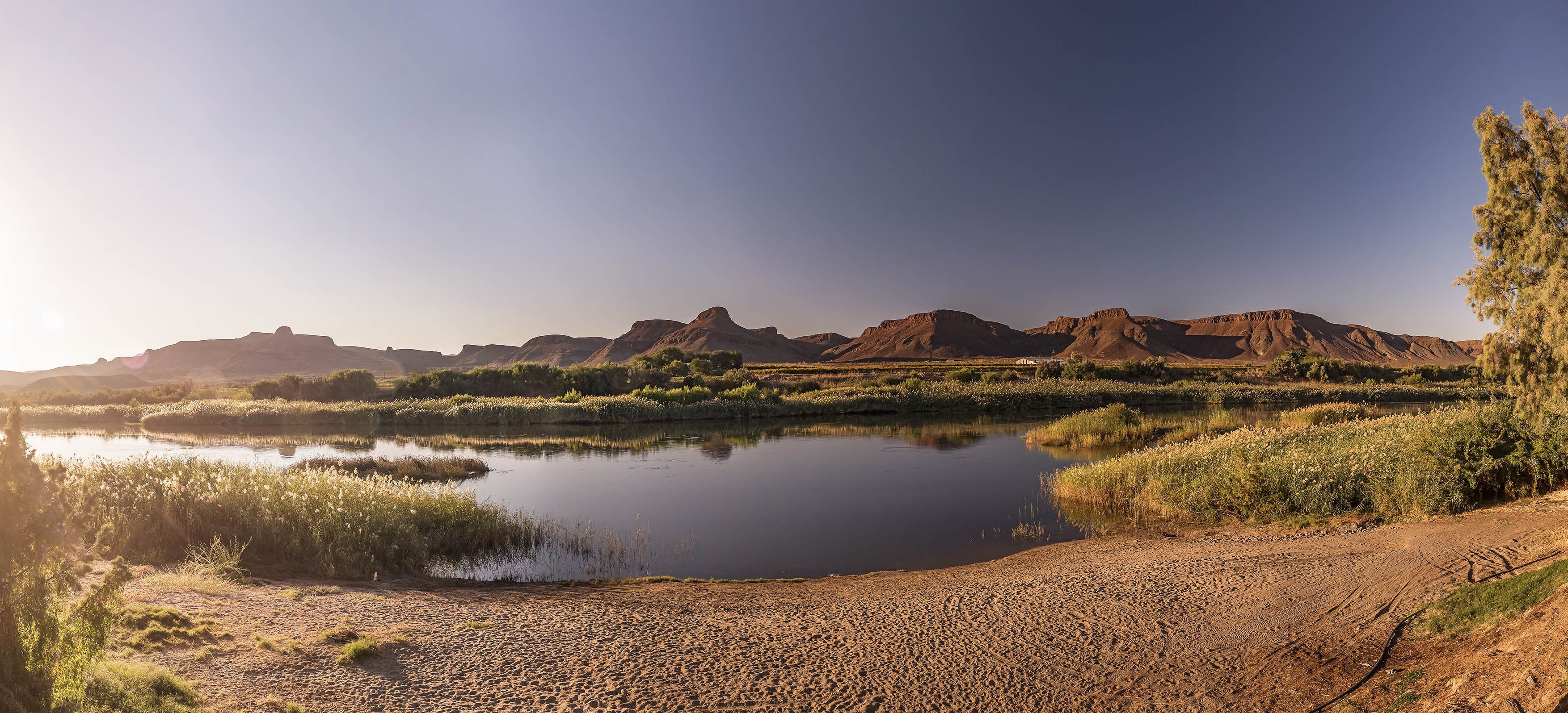 Wüstenlandschaft mit einem ruhigen See, sandigem Ufer und fernen Hügeln.