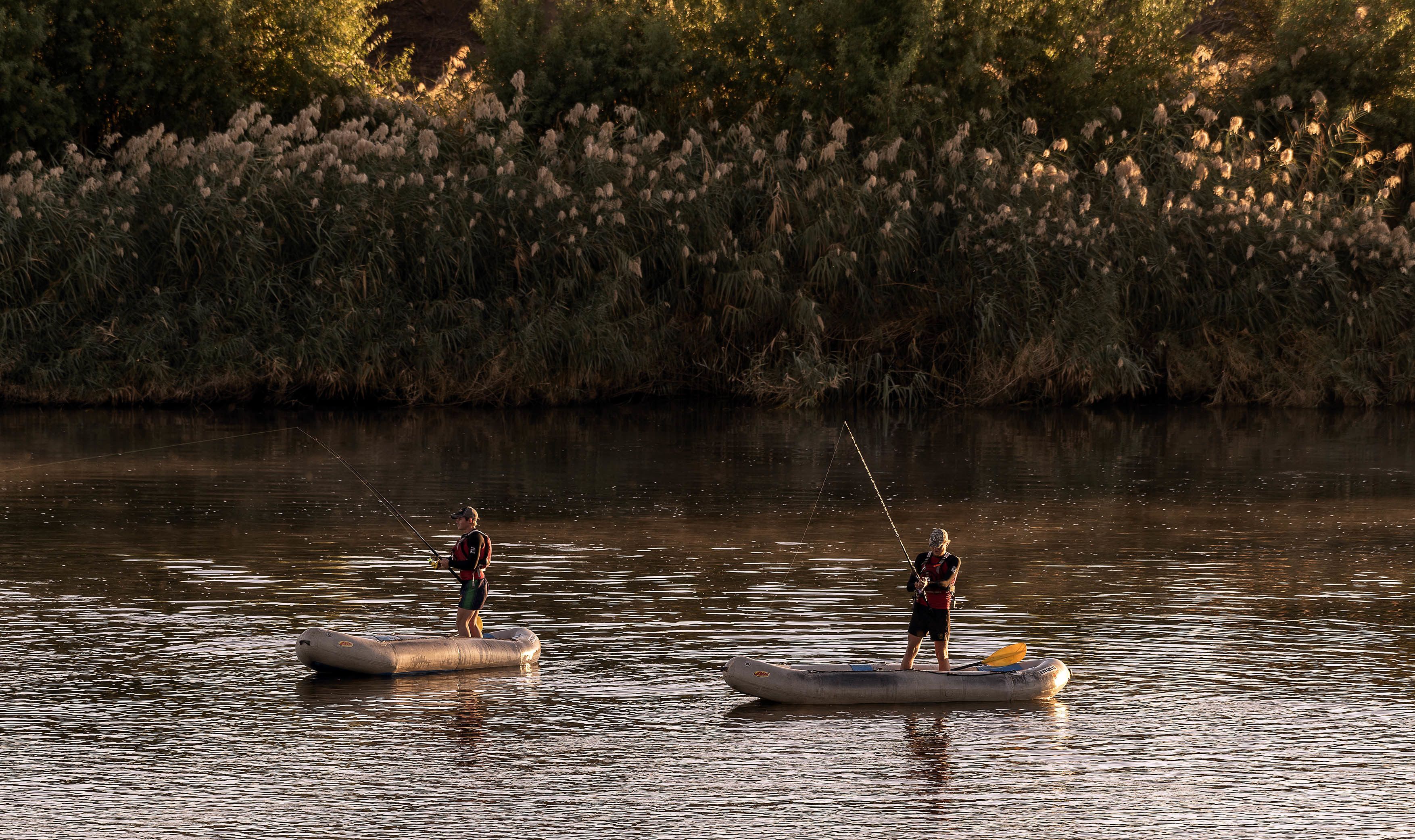 Deux personnes, à bord de radeaux gonflables, pêchent dans une rivière aux eaux calmes.
