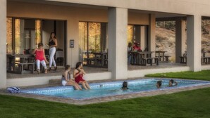A pool area with a tiled edge, outdoor seating, and a building with large windows. - Springbok Inn by Country Hotels (Nama Khoi)