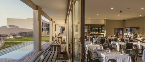 Un restaurant doté d’une terrasse offrant une vue sur une piscine, d’un bar et d’une vue sur un bâtiment à l’architecture moderne.