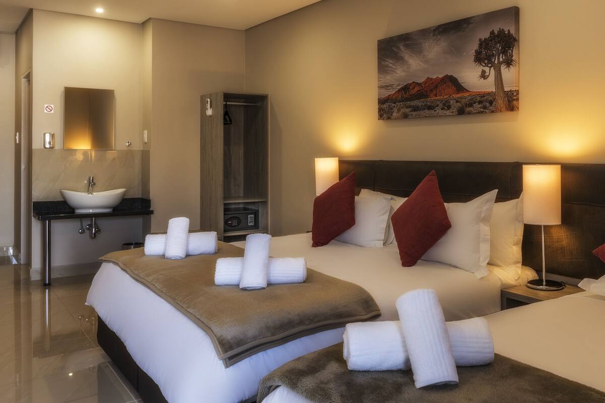 A hotel room with two beds, a bathroom, and a painting of a desert landscape.