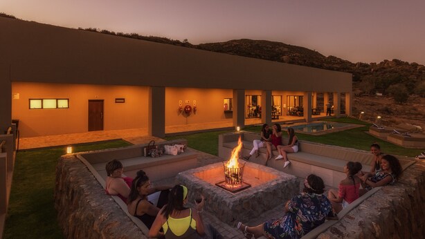 A group of people sitting around a fire pit in an outdoor area with a pool and a building in the background. - Springbok Inn by Country Hotels (Nama Khoi)
