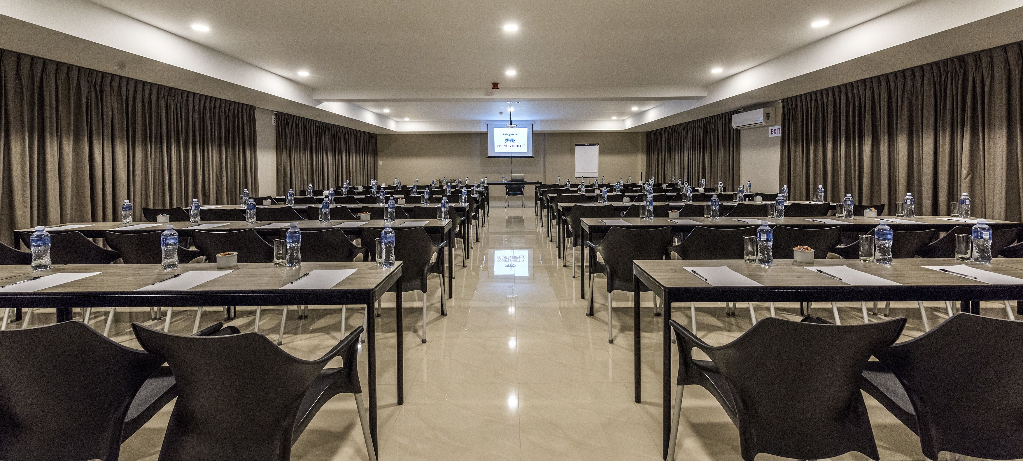 A conference room with rows of tables and chairs, equipped with water bottles and nameplates.