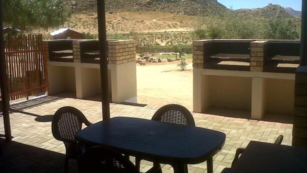 Eine Terrasse im Freien mit Tisch und Stühlen, einem Grill und Blick auf eine hügelige Landschaft.