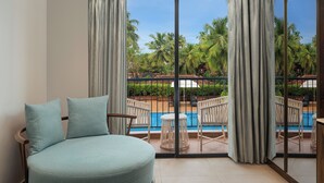 Una habitación con un ventanal grande, una cama redonda y vistas a una piscina y palmeras.