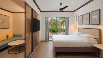 Habitación de hotel con cama, sofá, televisión, balcón con vistas a zonas verdes y ventilador de techo.