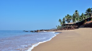 Una playa con cielos azules despejados, palmeras y un edificio con techo de paja.