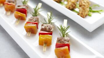 Une assiette rectangulaire blanche, sur laquelle sont présentées des brochettes de viande et de légumes, le tout garni de romarin.