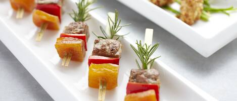 A white rectangular plate with skewers of meat and vegetables, garnished with rosemary.