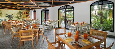 A restaurant with wooden tables and chairs, a tiled floor, and large windows with a view of greenery.