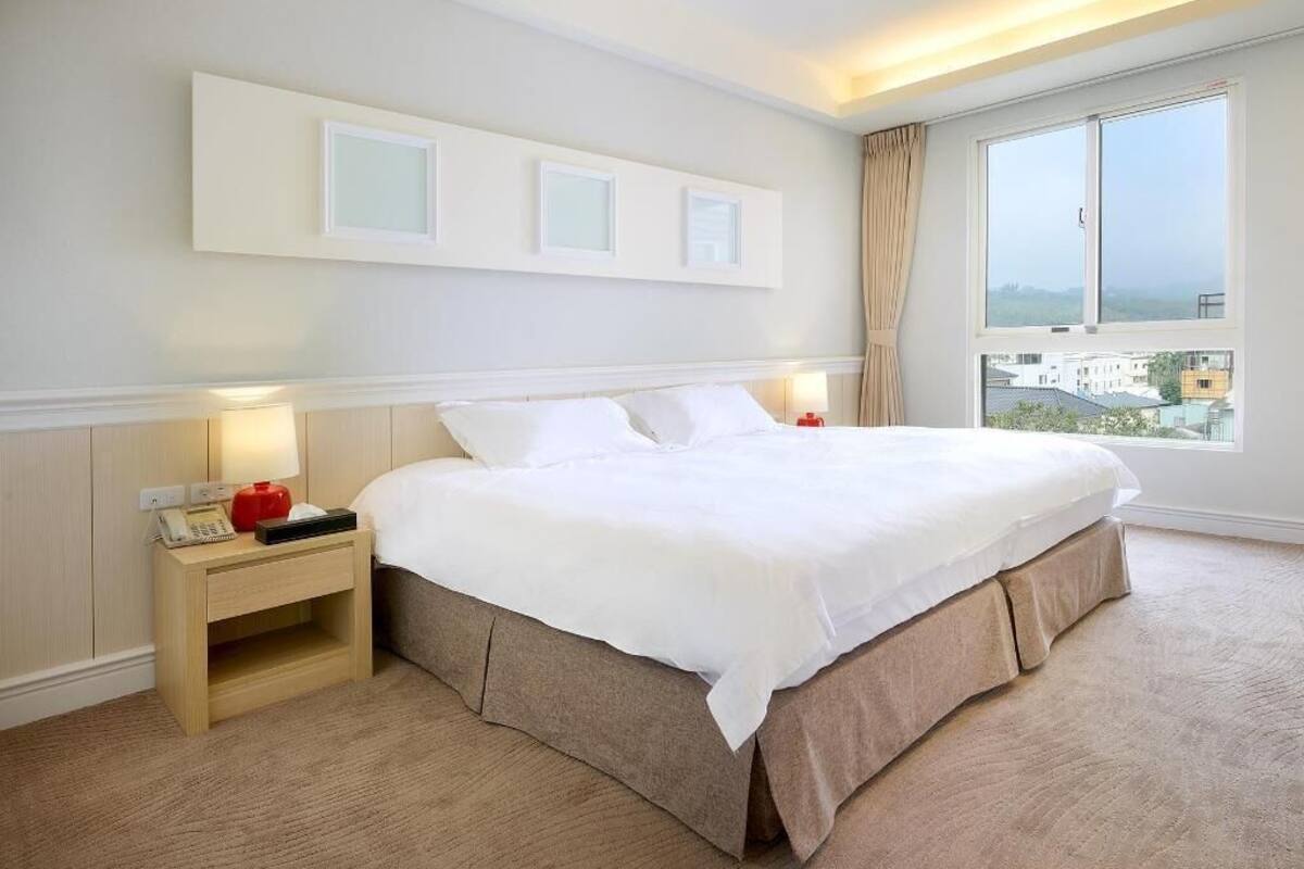 A hotel room with a large bed, bedside tables, a window with a view, and wall-mounted light fixtures.