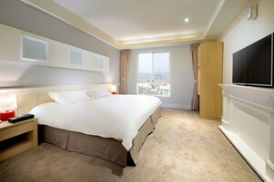 Quarto de hotel com cama grande, televisão, mesa de cabeceira e janela com cortinas.