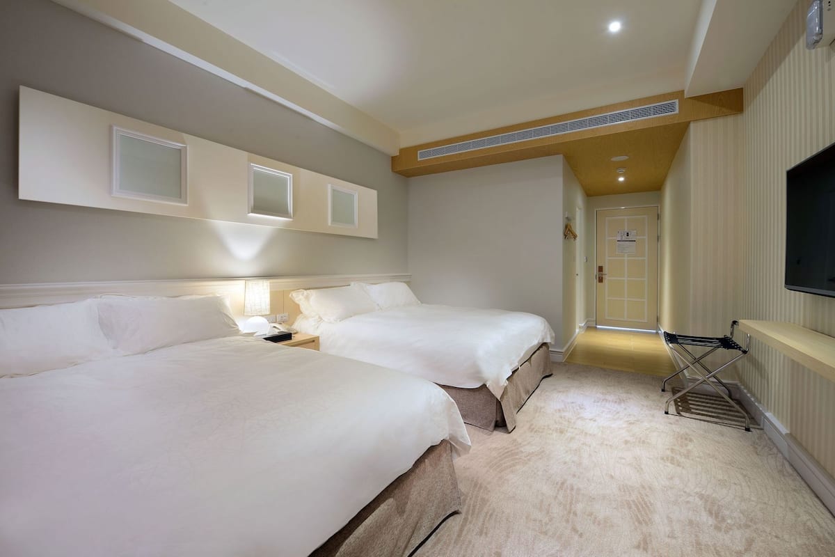 A hotel room with two beds, a TV, a desk, and a walk-in closet.