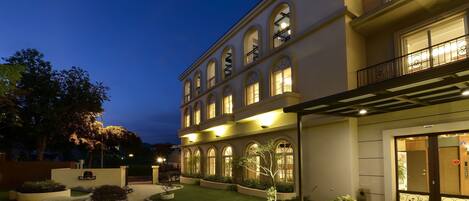 A multi-story hotel with a well-lit entrance, a landscaped garden, and a clear view of the building's architecture.
