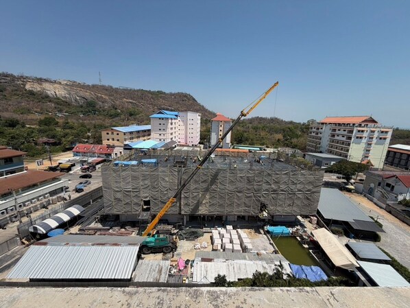 A construction site with a crane, buildings in the background, and a fenced area with construction materials. - The Precious (Hua Hin)