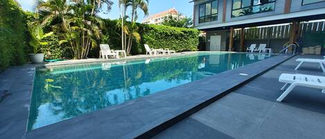 A modern hotel with a swimming pool surrounded by palm trees and lounge chairs.