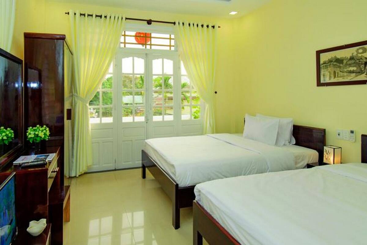 A hotel room with two beds, a TV, a desk with a computer, and a window with curtains.