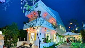 A two-story building with a balcony, illuminated by warm lighting, surrounded by greenery. - Minh Phat Homestay (Da Nang)