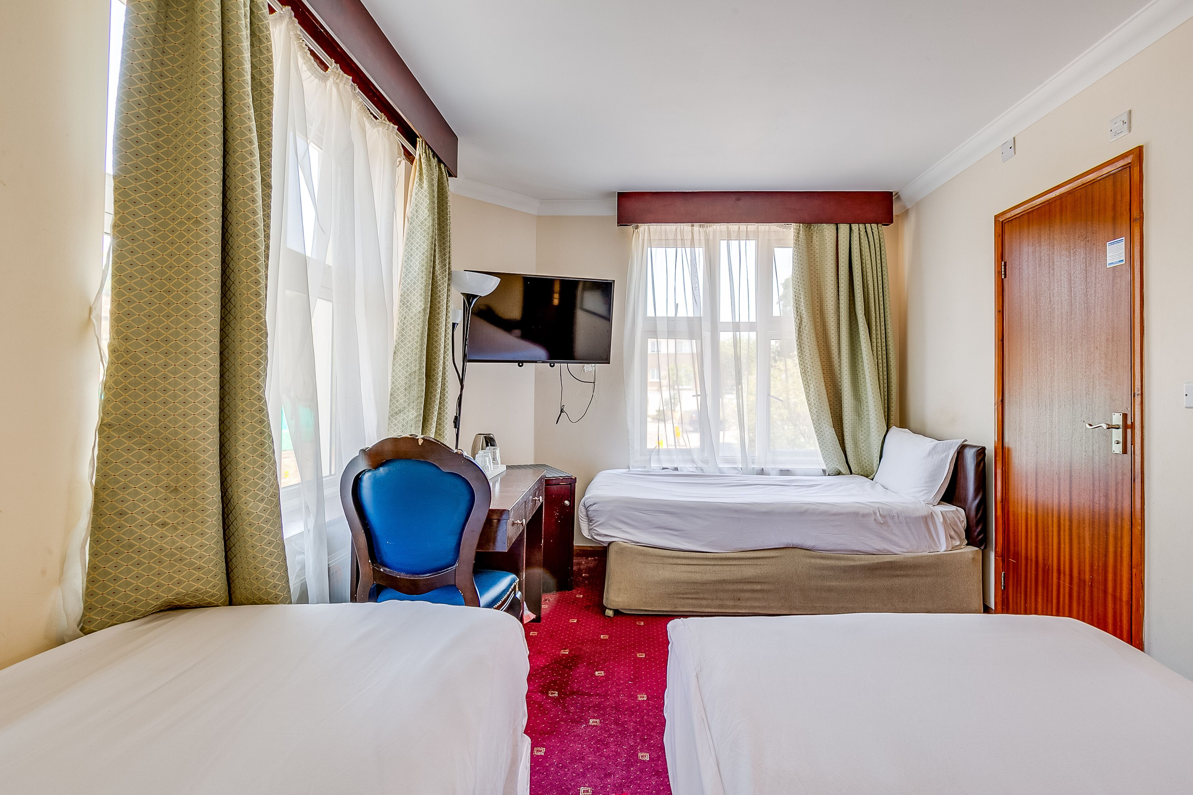 A hotel room with two beds, a desk with a chair, a TV, and a door.
