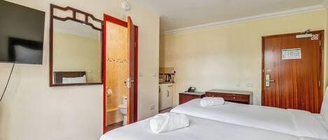 Una habitación de hotel con cama, televisión, baño y escritorio con teléfono.