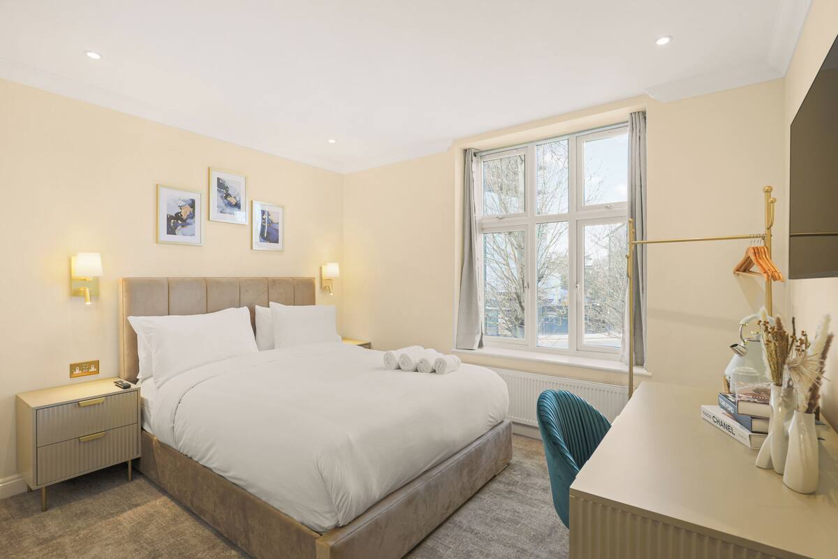 A neatly arranged bedroom with a large bed, bedside tables, a desk, and a window with curtains.