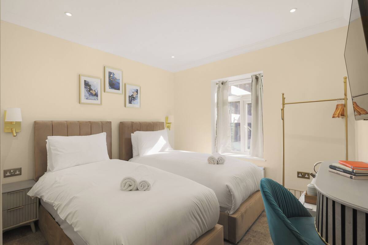A hotel room with two beds, a desk, a chair, and a window with curtains.