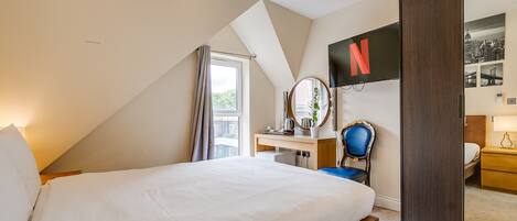 Una habitación de hotel moderna con una cama grande, un escritorio con una silla, un televisor montado en la pared y un armario.