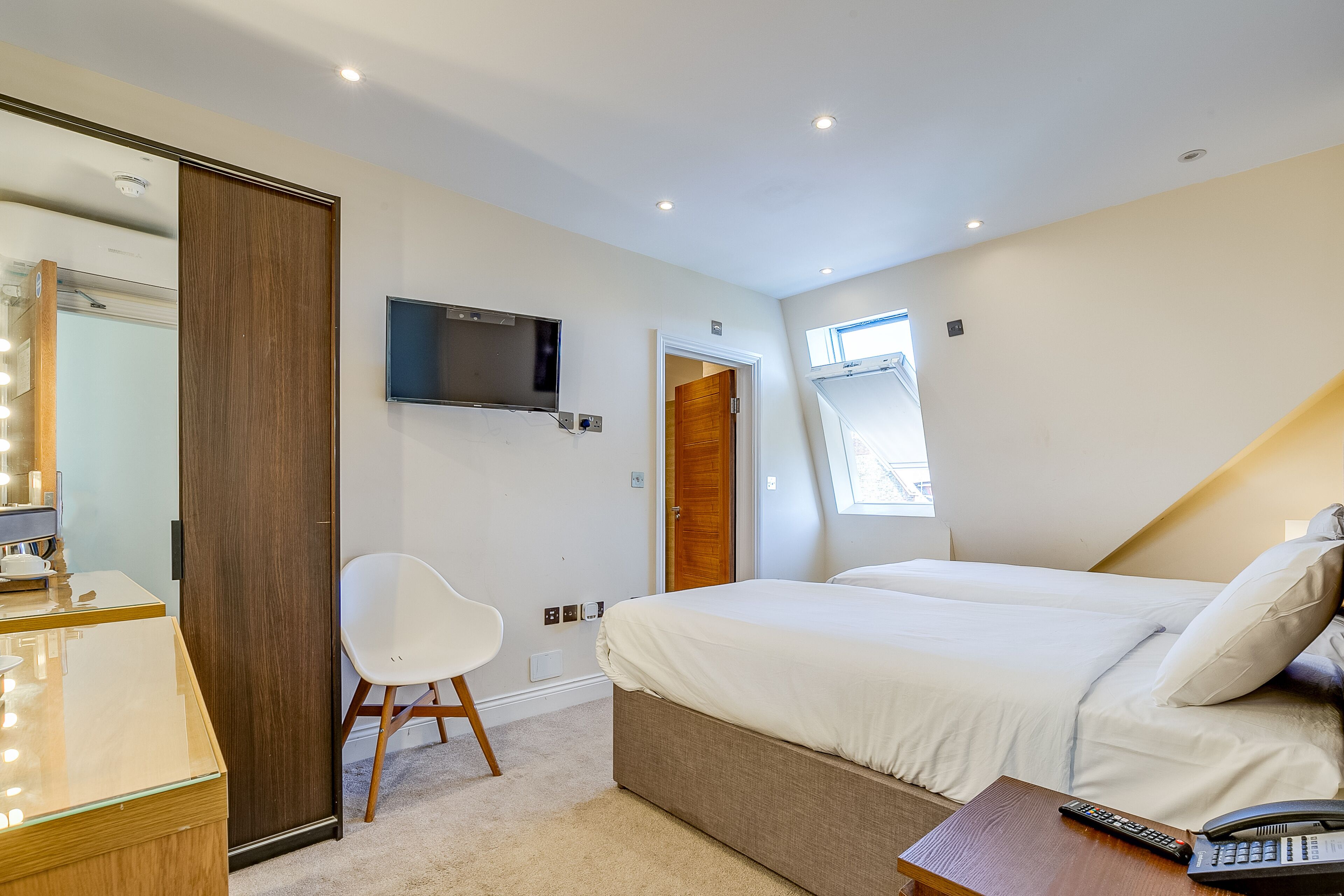 Un dormitorio con cama, escritorio con espejo, silla, televisión y ventana.