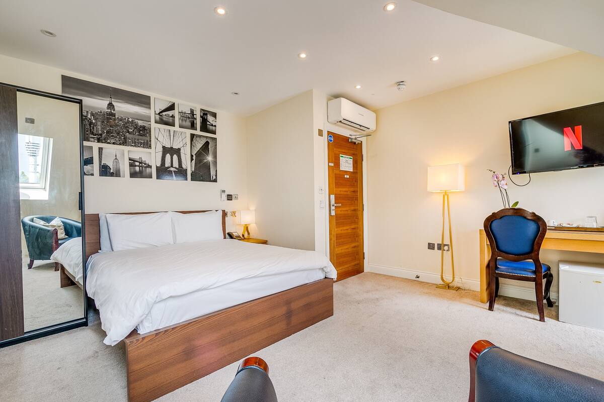 A hotel room with a bed, a desk with a chair, a TV, and a wall with pictures.