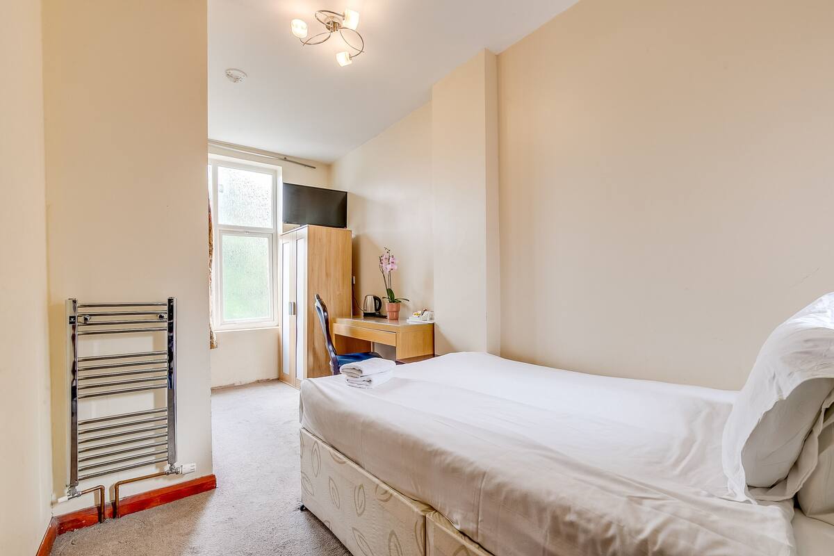 A bedroom with a bed, a desk, a chair, and a radiator.