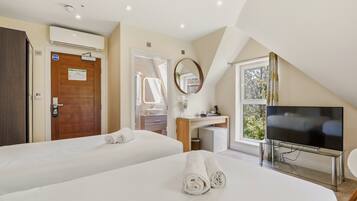 A hotel room with two beds, a TV, a bathroom, and a window with curtains.
